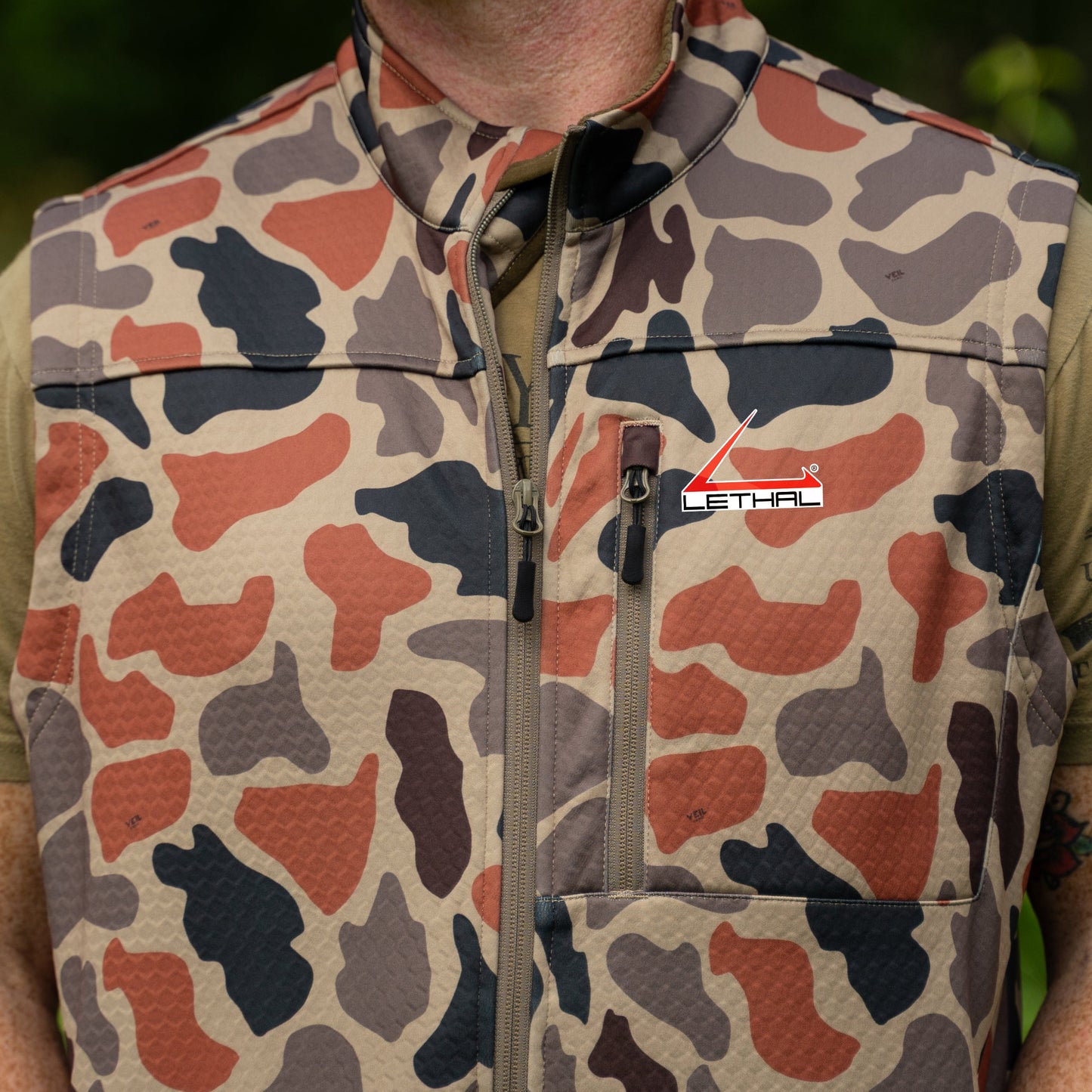 Person wearing a camouflage vest with a visible brand logo outdoors.